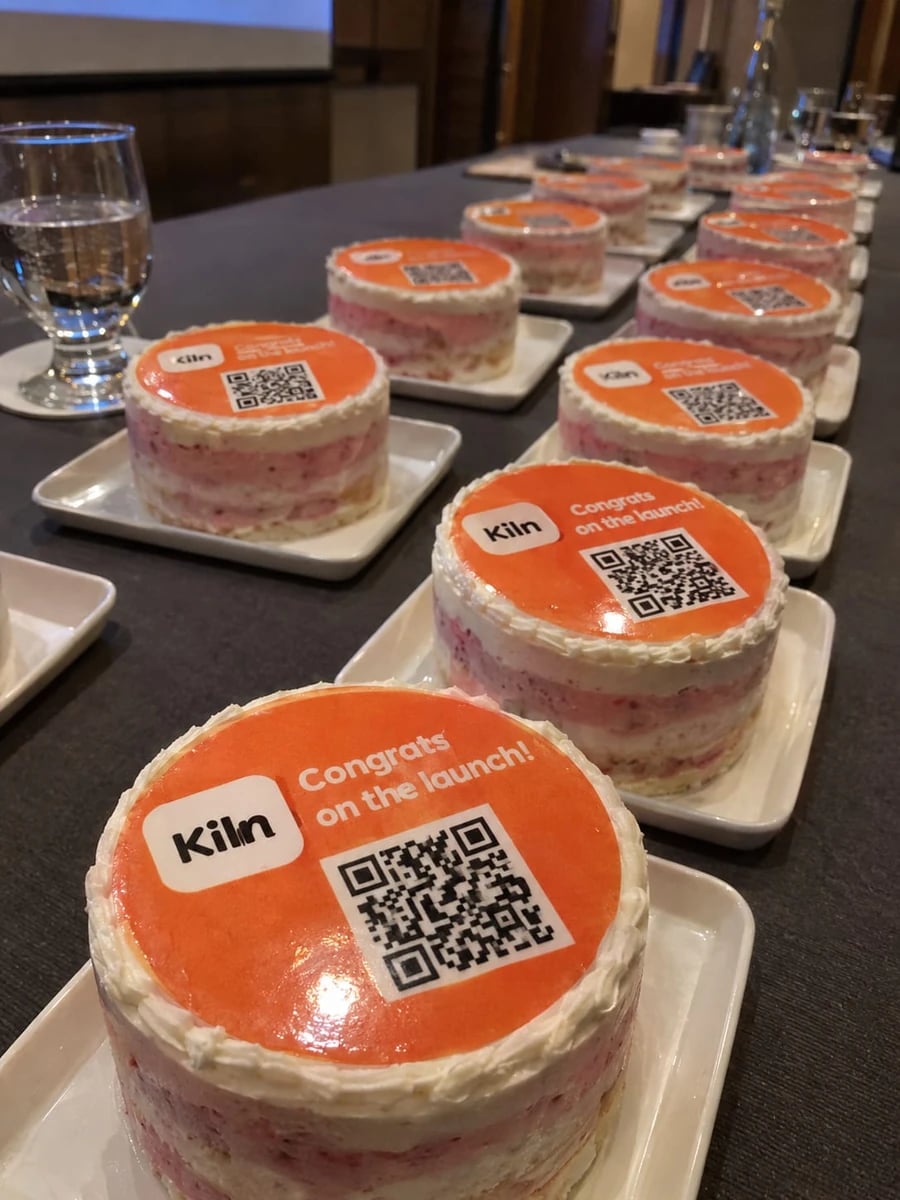 Rows of small cakes with a logo and QR code at an event